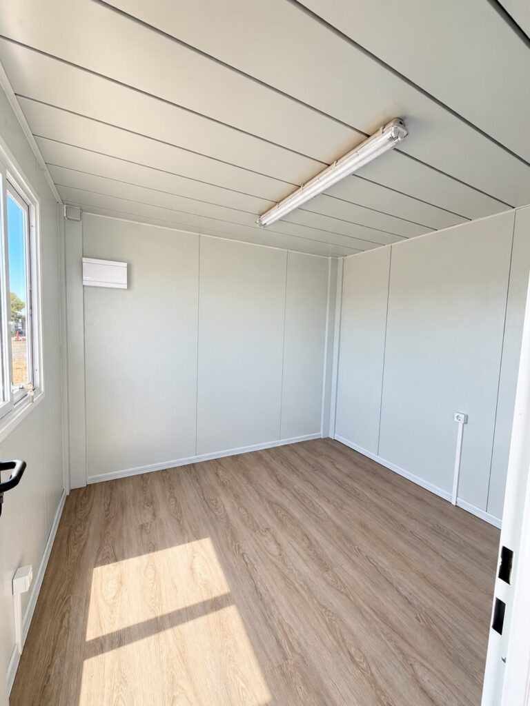 Interior de una oficina de obra prefabricada con suelo de madera y ventana